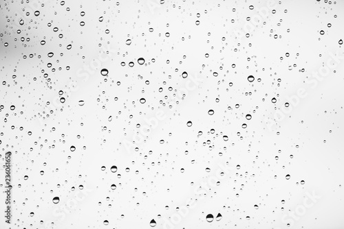 Dirty window glass with drops of rain. Atmospheric monochrome light background with raindrops. Droplets and stains close up. Detailed transparent texture in macro with copy space. Rainy weather.