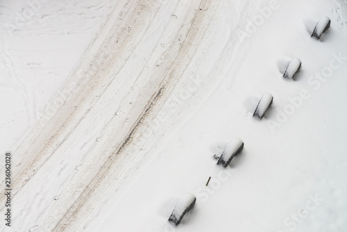 Snowy road. Fencing of old wheels. Fence from tires. Textured winter background. Abstract minimalist snowy weather texture. Car track in dirty snow. View from above. Traces of people and pets on snow.