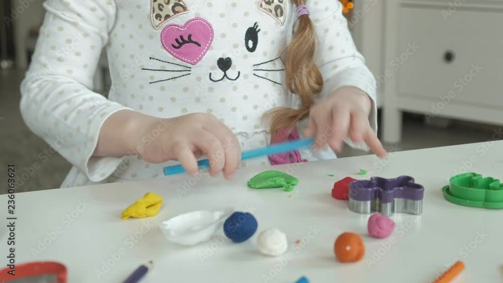 a little girl plays with plasticine, rolls balls, there are figures and colored pencils on the desktop, the development of fine motor skills of hands a little girl plays with plasticine, rolls balls, there are figures and colored pencils on the desktop, the development of fine motor skills of hands