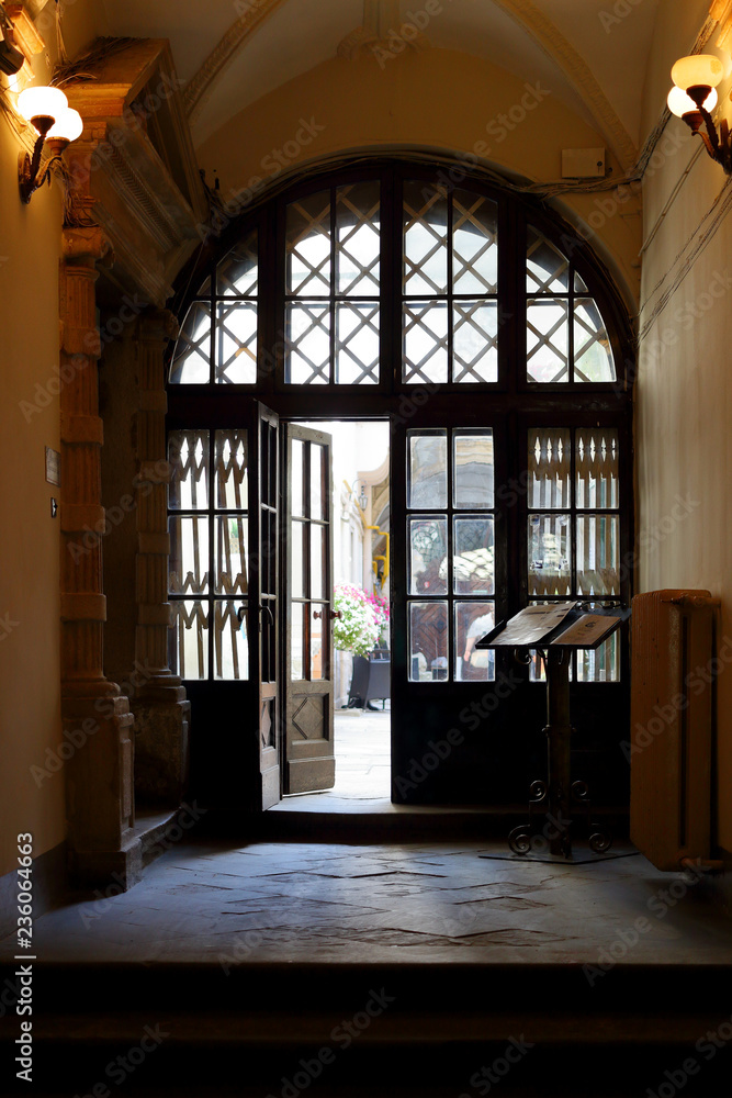 Passage through archway into corridor with entrance wooden door in brown tones. Indoors.