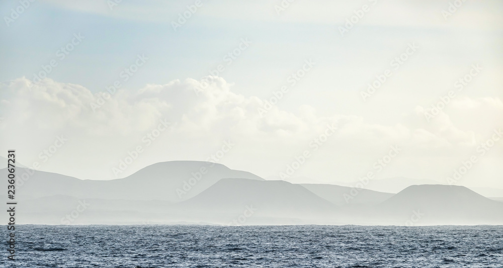 Mountain range in mist in the background and the Atlantic Ocean in the foreground. Fuerteventura, Canary Islands.