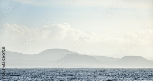 Mountain range in mist in the background and the Atlantic Ocean in the foreground. Fuerteventura  Canary Islands.