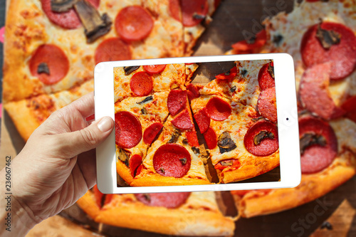closeup of hand holding holding tablet take photo of pizza on table