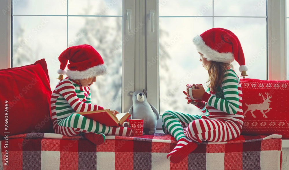 children girl and boy is sad on Christmas morning by the window. - obrazy, fototapety, plakaty 