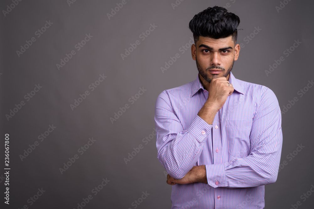 Young handsome Indian businessman against gray background