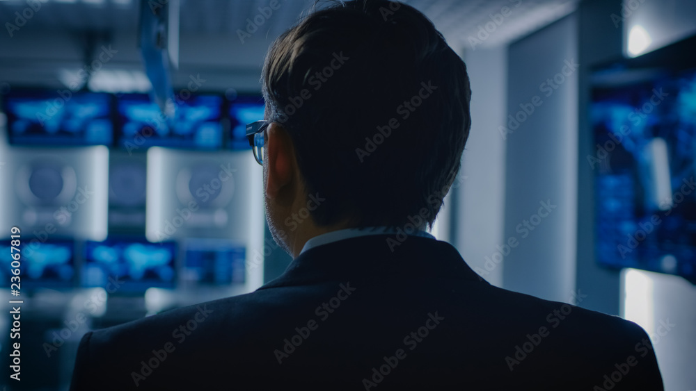 Back View Shot of the Government Official / Politician / Newsroom Reporter / Business Man Standing in the Room with Blurred Screens. Back View Shot of the Government Official / Politician / Newsroom Reporter / Business Man Standing in the Room with Blurred Screens.