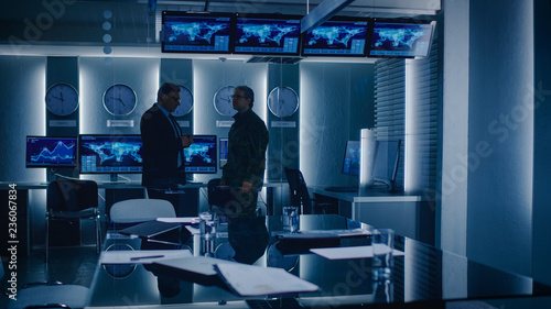 Federal Special Agent Talks To Military Man in the Monitoring Room. In the Background Busy System Control Center with Monitors Showing Data Flow. photo