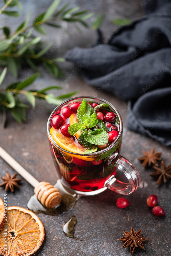 Hot spicy cranberry mulled wine or cranberry tea in glass cup decorated with orange peel and mint leaf Hot spicy cranberry mulled wine or cranberry tea in glass cup decorated with orange peel and mint leaf