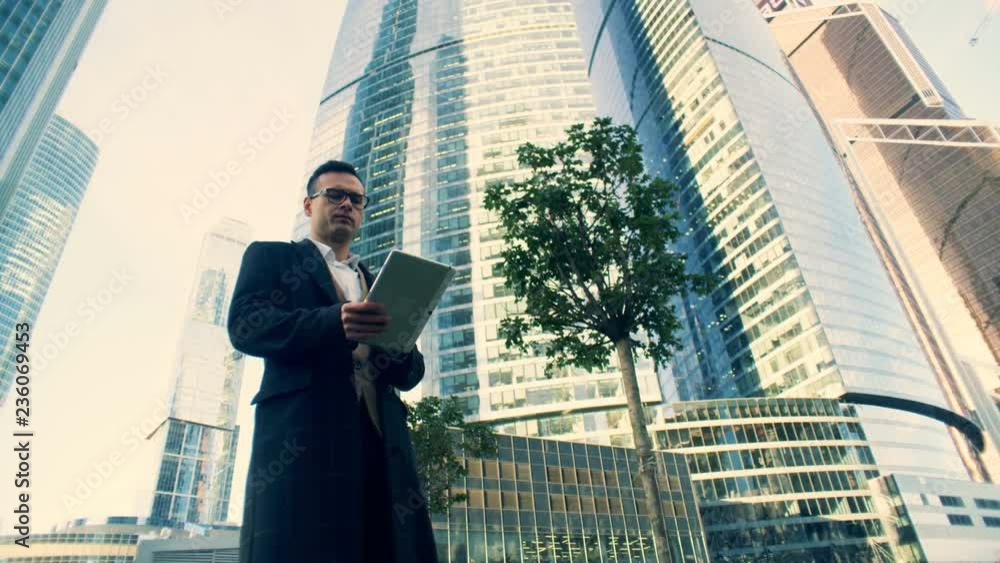 Businessman walks with a tablet near skyscrapers, close up. Businessman walks with a tablet near skyscrapers, close up.