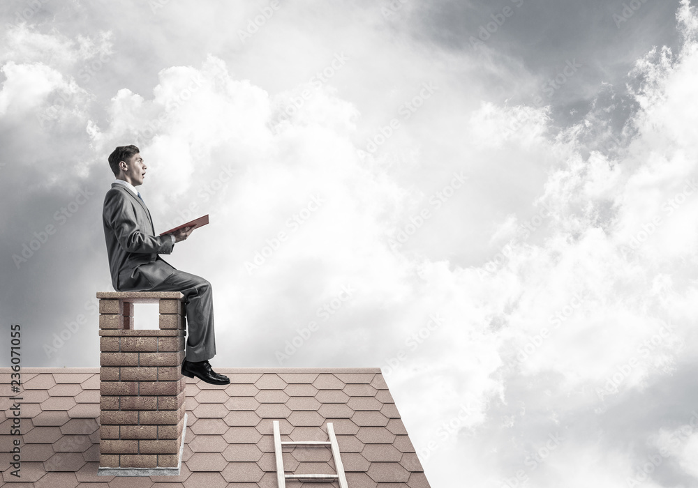 Student guy in suit on brick house roof reading book Student guy in suit on brick house roof reading book