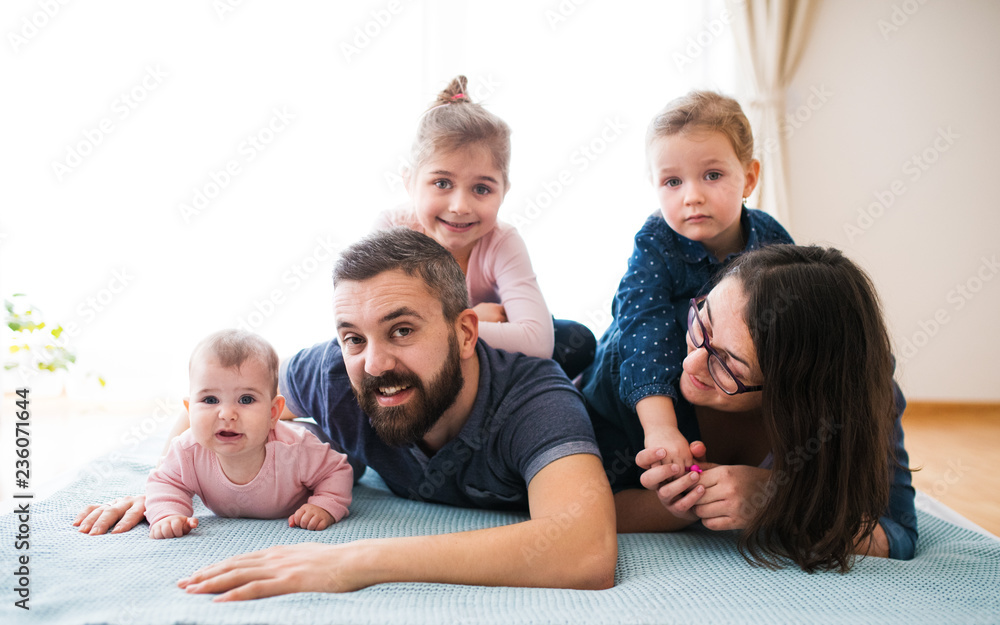 A portrait of young family with small children lying on floor indoors.