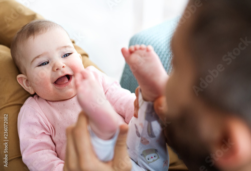 Unrecognizable father playing with baby daughter sitting indoors, having fun.