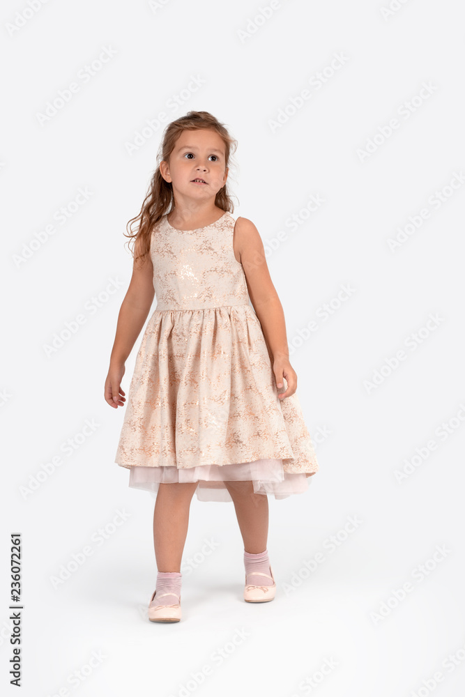 Full length portrait of a little smiling girl wearing beautiful beige elegant dress on a white background in the studio. Full length portrait of a little smiling girl wearing beautiful beige elegant dress on a white background in the studio.
