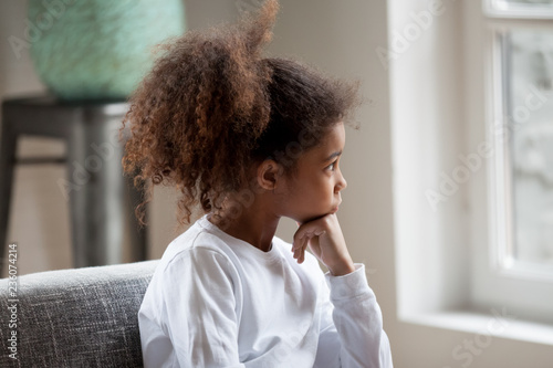 Fototapeta Thoughtful serious African American preschooler girl looking in window, pensive