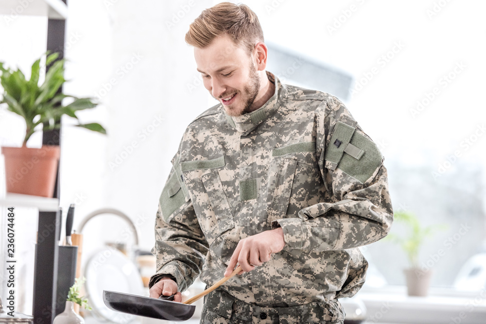 Fototapeta premium smiling army soldier cooking on pan in kitchen