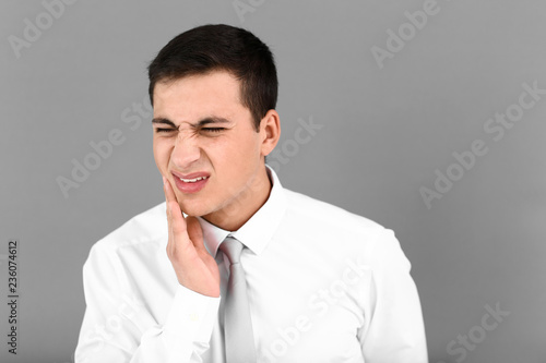 Young man suffering from toothache on grey background