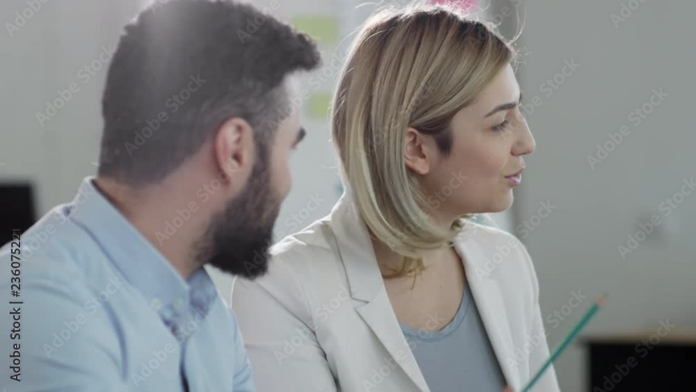 Young blonde businesswoman smiling and discussing project with male colleague during office meeting Young blonde businesswoman smiling and discussing project with male colleague during office meeting