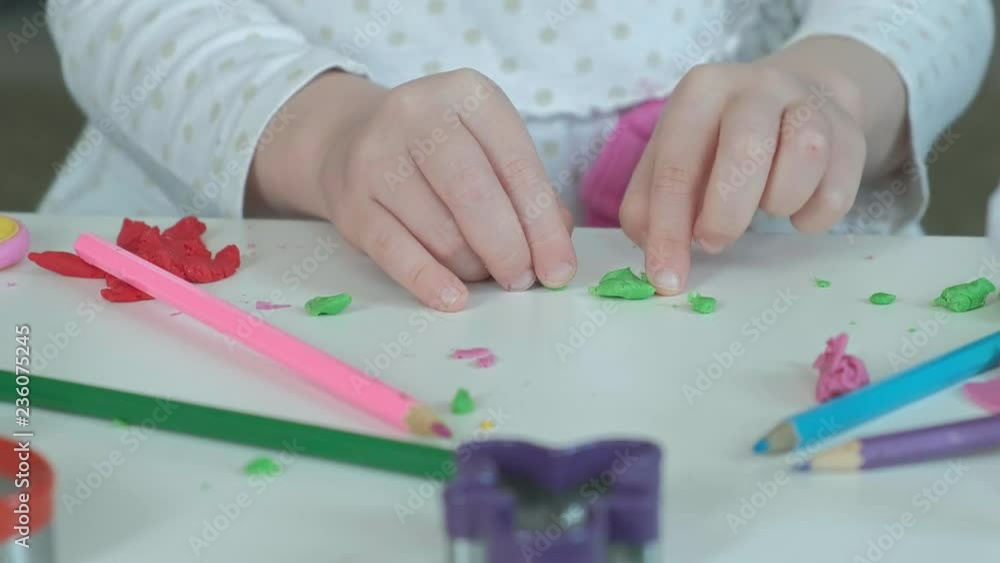 a little girl plays with plasticine, sculpts a figure, there are figures and colored pencils on the desktop, the development of fine motor skills of hands a little girl plays with plasticine, sculpts a figure, there are figures and colored pencils on the desktop, the development of fine motor skills of hands