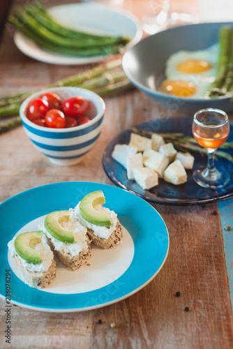 brunch of curd cheese sandwiches with avocado, tomatoes, brie and honey, boild green asparagus and fried eggs on the plate