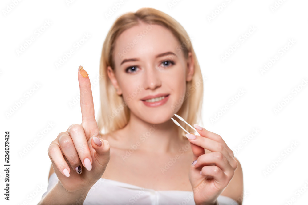 Focus on contact lens on finger of young woman. Young woman holding contact lens on finger in front of her face. Woman holding contact lens on white background. Focus on contact lens on finger of young woman. Young woman holding contact lens on finger in front of her face. Woman holding contact lens on white background.