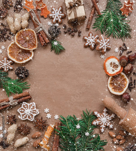 Frame with fir branches, Gingerbread cookies and Christmas decorations on dark brown paper background. Top view.