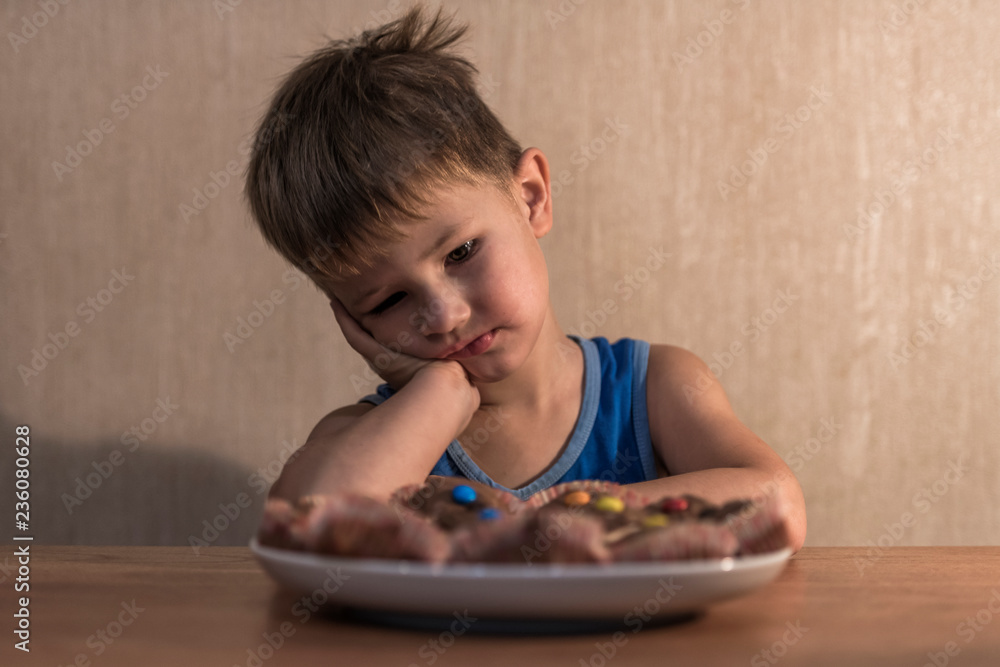 boy sits at the table and looks at the plate with cookies boy sits at the table and looks at the plate with cookies