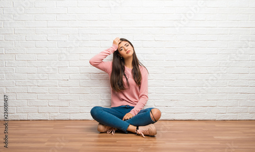 Teenager girl sitting on the floor in a room with an expression of frustration and not understanding