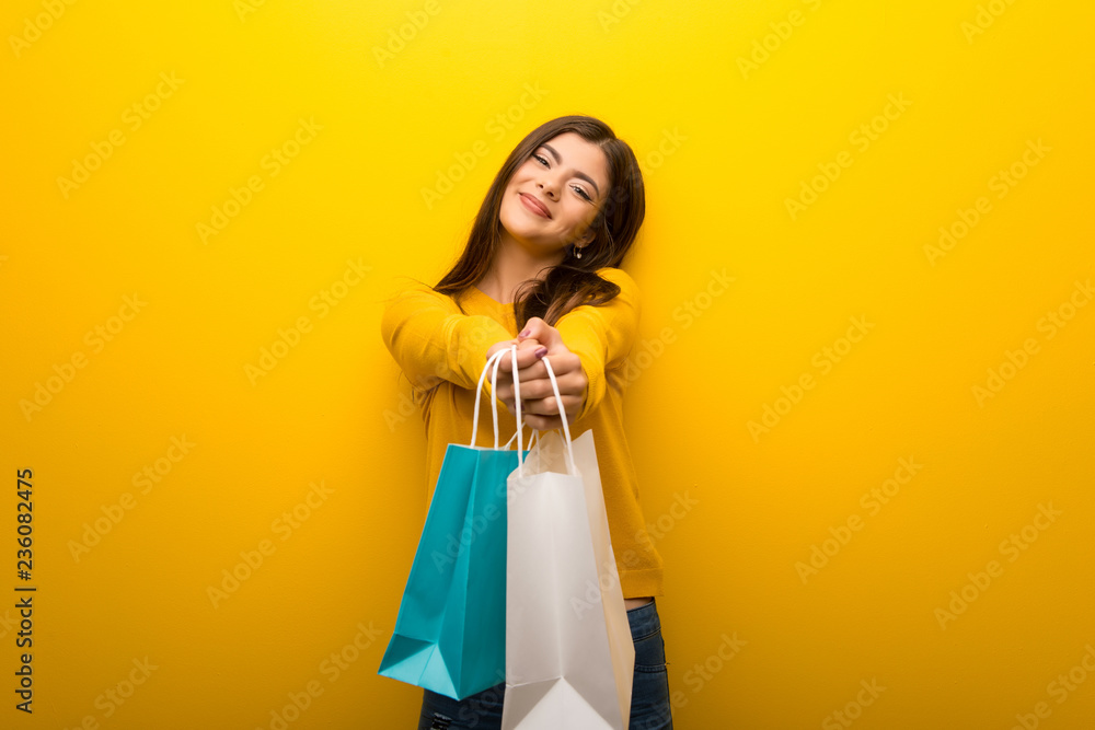 Teenager girl on vibrant yellow background holding a lot of shopping bags
