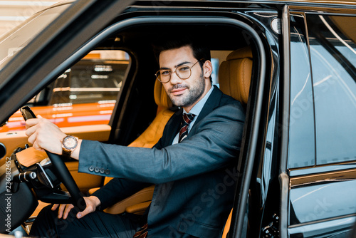 happy stylish businessman in eyeglasses sitting in luxury car