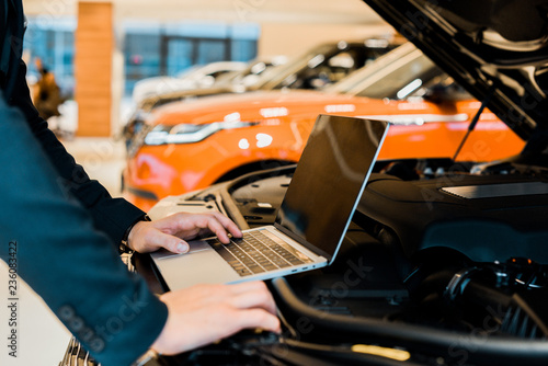 cropped image of businessman checking car hood with laptop with blank screen © LIGHTFIELD STUDIOS