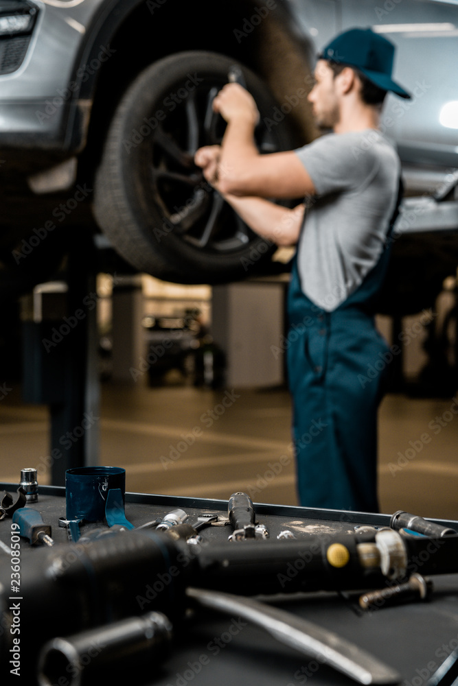 selective focus of auto mechanic in uniform fixing car wheel at auto repair shop