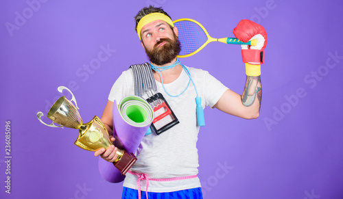Man bearded athlete hold sport equipment jump rope fitness mat boxing glove expander racket and golden goblet. Choose favorite sport. Sport concept. On way to achievement. Sport shop assortment © be free
