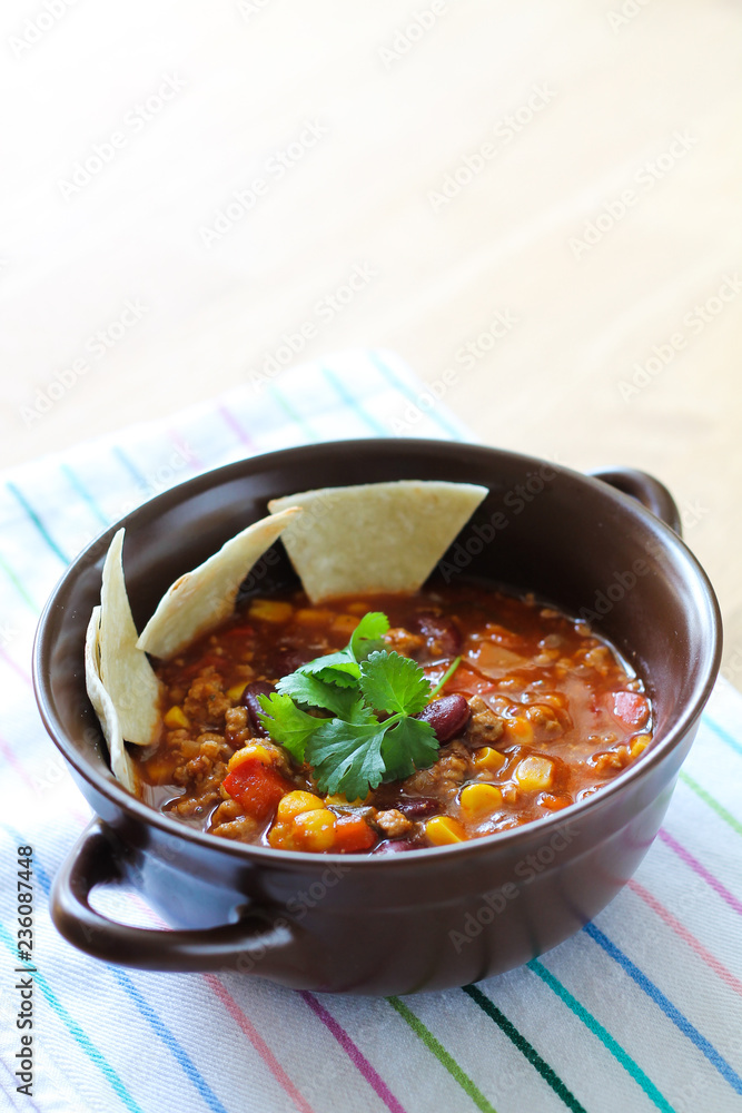Delicious chili con carne with tortilla in a clay bowl on wooden table Delicious chili con carne with tortilla in a clay bowl on wooden table
