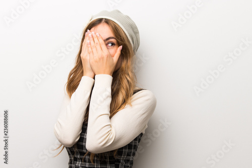 Fashionably woman wearing hat covering eyes by hands and looking through the fingers