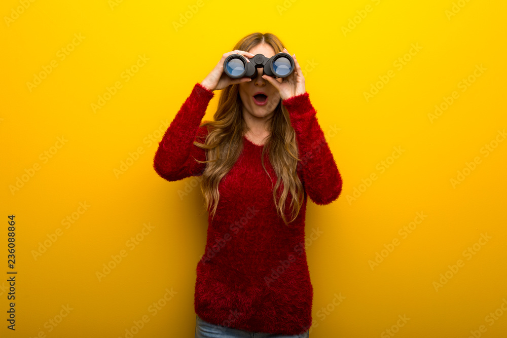 Young girl on vibrant yellow background and looking in the distance with binoculars