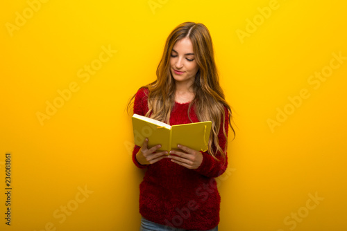 Young girl on vibrant yellow background holding a book and enjoying reading