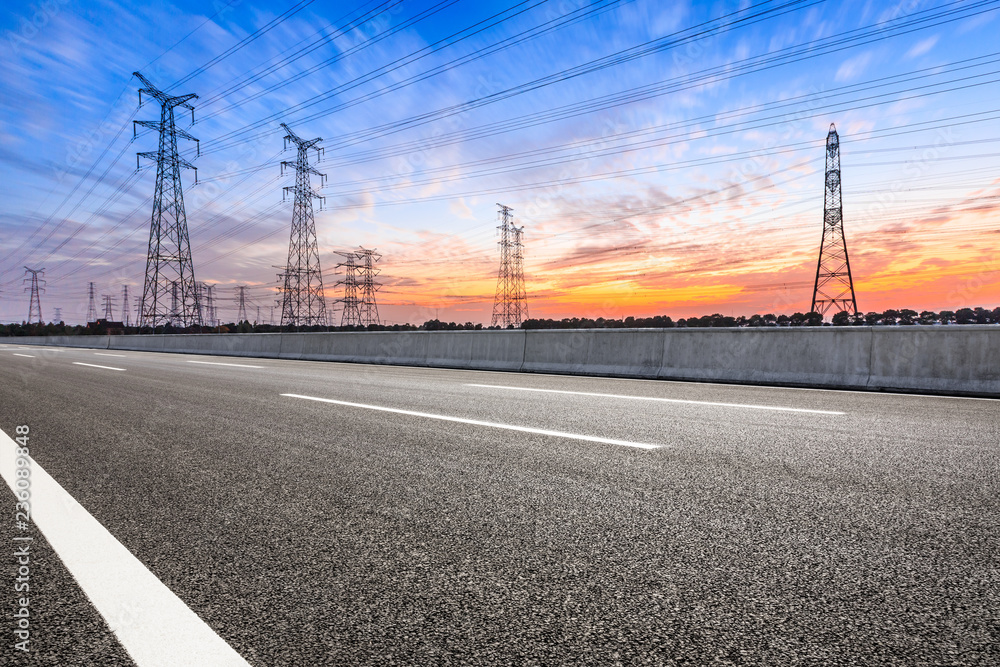 Asphalt road and high voltage power towers at sunset