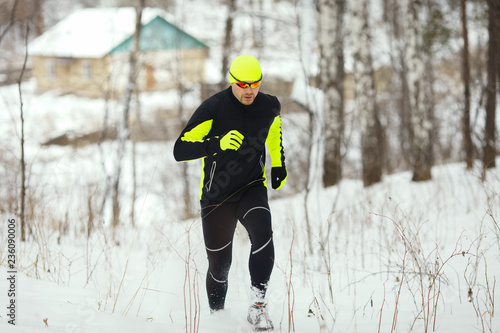 An athlete in sports clothes runs in a snow-covered forest.