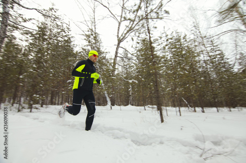 An athlete in sports clothes runs through deep snow in a snow-covered forest.