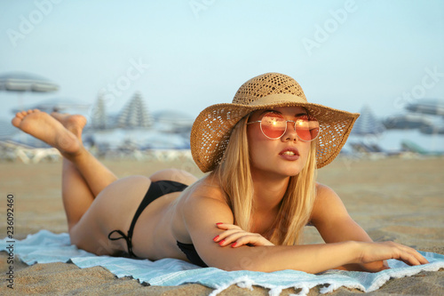 girl tanning on the beach. sexy blonde girl in black bikini, sunglasses and  hat with beach on background. Stock Photo | Adobe Stock