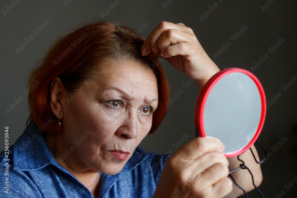 Naklejka premium Elderly woman looking at gray hair in her hair looking in the mirror