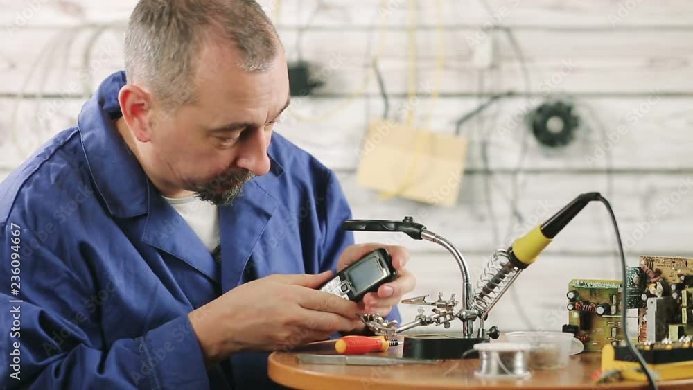 the engineer is engaged in repair of the old mobile phone the engineer is engaged in repair of the old mobile phone