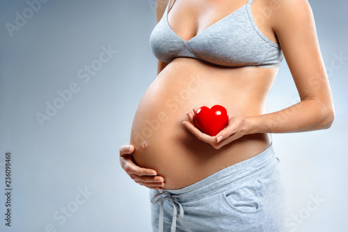 Wallpaper Mural Close up of pregnant woman holding red heart on grey background. Pregnancy, maternity, preparation and expectation concept Torontodigital.ca