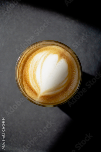 Close up coffee cup with heart shape latte art foam on black table.