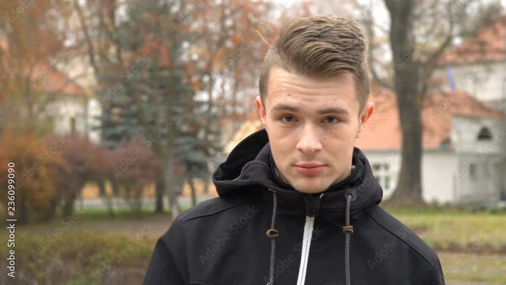 A young man smokes a cigarette and lets go of smoke outside on a cold autumn day. A young man smokes a cigarette and lets go of smoke outside on a cold autumn day.