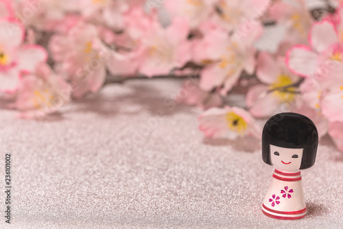 Japanese New Year's Cards with little doll Kokeshi with flower pattern on a glitter silver background with a branch of cherry blossoms flowers. photo