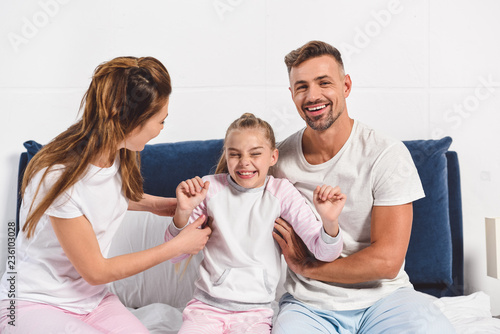 Foto smiling parents tickling preteen daughter in bed