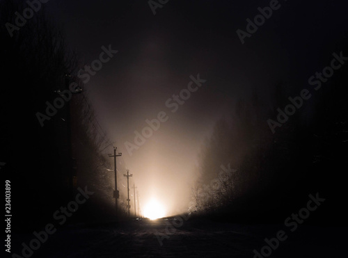 Light at the end of a road on a misty winter night, gloomy isolated atmosphere