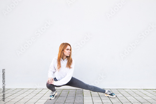 Young sports girl doing stretchings on the background of a white wall. Street morning training on a white background. Copyspace