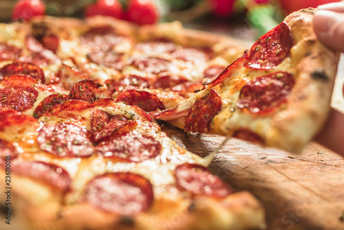 Hot pizza slice with melting cheese on a rustic wooden table.